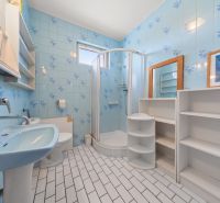 Ein Badezimmer mit blauen Fliesen, einer Duschkabine und weißen Möbeln in einem Einfamilienhaus.