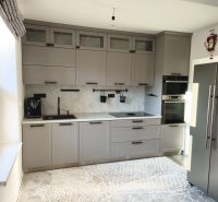 Küche in einem Einfamilienhaus mit grauen Schränken und gemustertem Teppich auf einem Boden in Holzoptik.