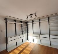 Ein Kleiderschrank im Einfamilienhaus mit Regalen, Schubladen und einem Boden in Holzoptik.