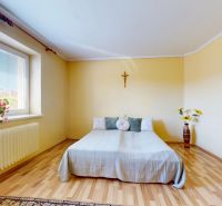 Schlafzimmer im Einfamilienhaus mit einfachem Bett, Holzelementen und Blumen am Fenster.