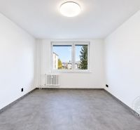 Ein geräumiges Zimmer mit Fenster, Heizkörper und einem Boden mit Holzdekor in einer 2-Zimmer-Wohnung.