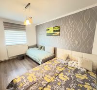 Ein Schlafzimmer in einem Einfamilienhaus mit einem Boden in Holzoptik und einer gemusterten Tapete an der Wand.