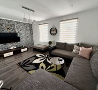 Wohnzimmer in einem Einfamilienhaus mit Holzboden, großem Sofa und gemustertem Teppich.