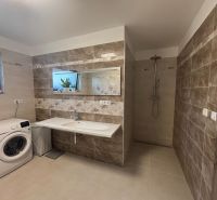 Badezimmer im Einfamilienhaus mit Waschmaschine, hellem Fliesenbelag und Duschkabine.