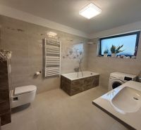Ein Badezimmer in einem Einfamilienhaus mit Badewanne, Waschbecken und Waschmaschine in sanften Beigetönen.