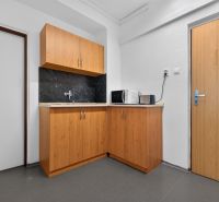 Büroküche mit Schränken, Spüle, Mikrowelle und Toaster auf einem Boden mit Holzdekor.