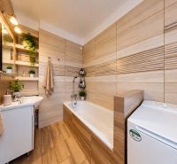 Badezimmer mit Badewanne, Waschbecken und Pflanzen in einer 3-Zimmer-Wohnung, Boden mit Holzdekor.