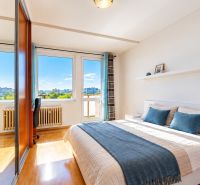 Helles Schlafzimmer mit Bett, Spiegelschrank und Boden in Holzoptik.