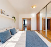 Schlafzimmer in einer 3-Zimmer-Wohnung mit einem großen Bett und einem Spiegelschrank, Boden mit Holzdekor.
