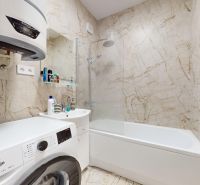 Badezimmer in einer 2-Zimmer-Wohnung mit Waschmaschine, Waschbecken und Badewanne.