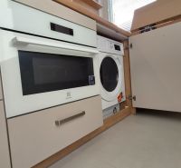 Eine eingebaute Waschmaschine und ein Backofen in der Küchenzeile einer Einzimmerwohnung mit hellem Boden.