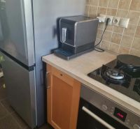 Küche in einer 3-Zimmer-Wohnung mit Kühlschrank, Herd und Kaffeemaschine auf einer Steinarbeitsplatte.