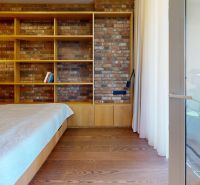 Schlafzimmer in einer 2-Zimmer-Wohnung mit Ziegelwand und Boden in Holzoptik.