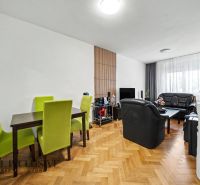 Wohnzimmer mit schwarzen Sofas, Esstisch und Holzboden.