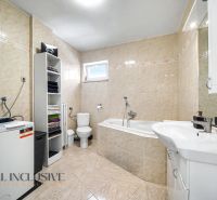 Ein Badezimmer in einem Einfamilienhaus mit einer Badewanne, einem Waschbecken, einer Waschmaschine und einem Regalschrank.