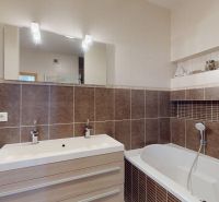 Ein Badezimmer mit einem hellen Waschbecken und einer Badewanne in einer 4-Zimmer-Wohnung, ergänzt durch braune Fliesen.