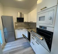Küche mit eingebautem Backofen, weißen Schränken und Holzboden in einer Zweizimmerwohnung.
