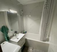 Badezimmer in einer 2-Zimmer-Wohnung mit Badewanne, Waschbecken, Waschmaschine und Fliesen.
