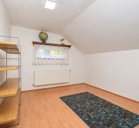 Ein Zimmer in einem Einfamilienhaus mit einem Boden in Holzoptik, einem Regal und einem Fenster.