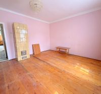 Ein Zimmer in einem Einfamilienhaus mit einem Kachelofen und einem Boden in Holzoptik.
