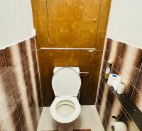 Toilette in einer 3-Zimmer-Wohnung mit braunen Fliesen und einer Fußmatte.