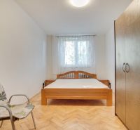 Schlafzimmer in einer 2-Zimmer-Wohnung mit einem Doppelbett, einem Stuhl und einem Boden mit Holzdekor.