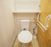 Ein kleines Badezimmer in einer 2-Zimmer-Wohnung mit Toilette, weißen Wänden und Rohren an der Seitenwand.