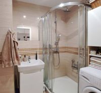 Badezimmer mit Waschbecken, Dusche und Waschmaschine in einer 3-Zimmer-Wohnung, beigefarbene Fliesen.