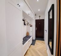 Der Flur in einer 3-Zimmer-Wohnung mit einem Boden in Holzoptik und weißen Aufbewahrungsschränken.
