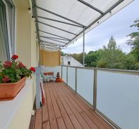 Ein Balkon in einer 3-Zimmer-Wohnung mit Holzboden, Blumen und Aussicht.