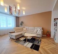 Wohnzimmer in einer 3-Zimmer-Wohnung mit einem weißen Sofa und einem Boden in Holzoptik.