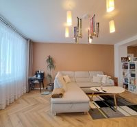 Wohnzimmer mit weißem Sofa, Holzboden und Bücherregal in einer 3-Zimmer-Wohnung.