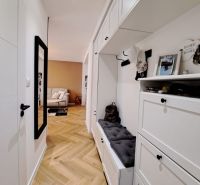 Der Flur in einer 3-Zimmer-Wohnung mit weißen Möbeln und einem Boden in Holzoptik.