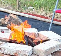 Eine Feuerstelle, umgeben von Ziegeln und Stühlen, im Garten eines Einfamilienhauses.