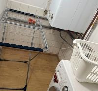 Waschküche in einem Einfamilienhaus mit Waschmaschine, Wäscheständer und Boden mit Holzdekor.