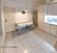 Küche in einer 2-Zimmer-Wohnung mit weißen Schränken, Tisch und Fliesen.