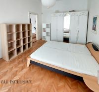 Schlafzimmer in einer 2-Zimmer-Wohnung mit Holzboden, Bett, Schrank und Regalen.