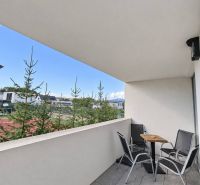 Balkon einer 2-Zimmer-Wohnung mit Sitzgelegenheit, Blick ins Grüne und modernem Fliesenboden.
