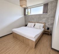 Schlafzimmer in einer 2-Zimmer-Wohnung mit Bett, grauer Wand und Boden in Holzoptik.