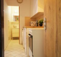Kochnische in einem Einzimmerapartment mit weißen Schränken und Geräten, Fliesenboden.