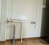 Rohre und Steckdose in einem Innenraum mit Holzboden.