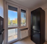 Eine Küche mit weißen Wänden, großen Fenstern und einem schwarzen Kühlschrank in einer 3-Zimmer-Wohnung.