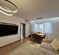 Wohnzimmer in einer 3-Zimmer-Wohnung mit einem großen Fernseher, einem Boden in Holzoptik und einem Esstisch.