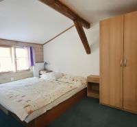 Schlafzimmer in der Ferienwohnung mit Holzbalken, Schrank und Bett neben dem Fenster.