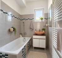 Ein Badezimmer in einem Einfamilienhaus mit grauen Fliesen, einer Badewanne und einem Waschbecken auf einem Schrank.