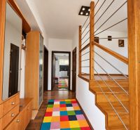 Innenraum eines Einfamilienhauses mit einer Treppe aus Holzdekor und einem bunten Teppich.