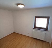 Ein Zimmer in einem Einfamilienhaus mit einem Boden in Holzoptik und einem Fenster mit Heizkörper.