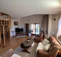 Wohnzimmer in einem Einfamilienhaus mit einem bequemen Sofa, einer Treppe und einem Boden in Holzoptik.