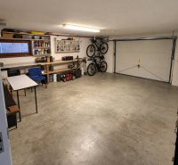 Eine Garage in einem Einfamilienhaus mit Klapprädern, einem Rasenmäher und Regalen für Werkzeuge.