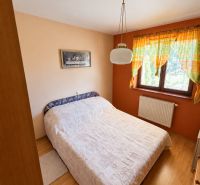 Schlafzimmer in einem Einfamilienhaus mit Bett, Vorhängen und Bodenbelag in Holzoptik.